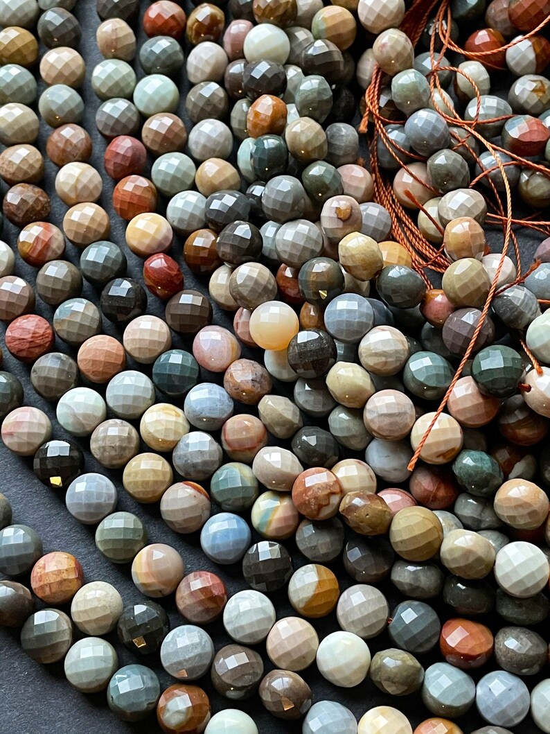 May include: A strand of faceted gemstone beads in various shades of brown, grey, and blue. The beads are round and have a smooth, polished finish.