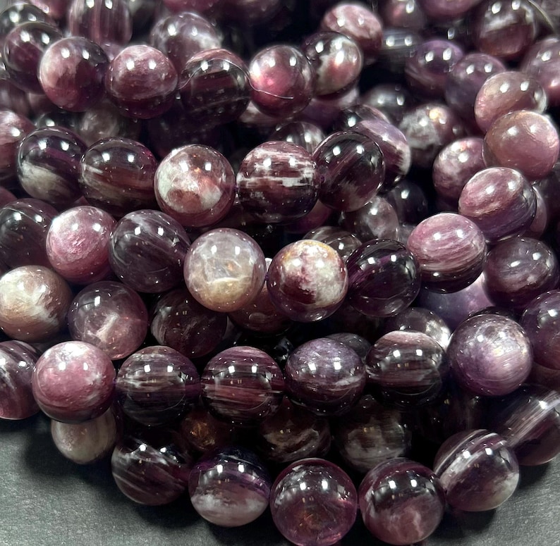K&ouml;nnte beinhalten: Eine Str&auml;hne aus violetten und wei&szlig;en, gestreiften Edelsteinperlen. Die Perlen sind rund und haben eine glatte, polierte Oberfl&auml;che.
