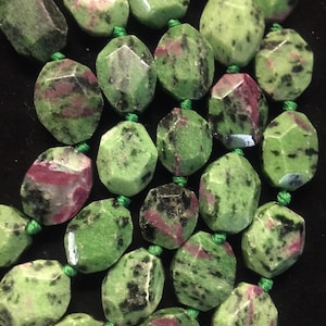May include: A strand of green, black, and pink gemstone beads. The beads are faceted and have a natural, irregular shape.