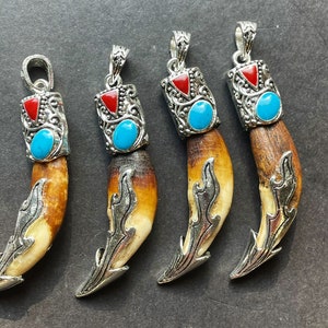 May include: Four silver pendants shaped like animal teeth with intricate designs and turquoise and red accents.