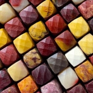 May include: A close-up of a collection of colorful, faceted gemstone beads. The beads are arranged in a grid pattern and feature a variety of colors, including red, yellow, brown, and white.