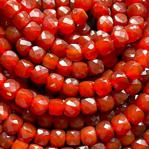 May include: A strand of red carnelian beads, each bead is faceted and has a square shape.