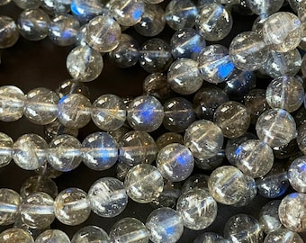 May include: A strand of gray labradorite gemstone beads with iridescent blue flashes. The beads are round and smooth, and they are strung on a clear thread.