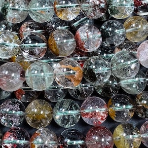 Op de afbeelding: Een streng ronde, heldere, veelkleurige edelsteen kralen. De kralen hebben insluitsels van groen, rood en goud. De kralen zijn geregen op een heldere draad.