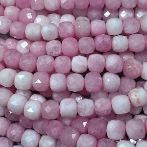 Puede incluir: Una hebra de cuentas de piedras preciosas facetadas de color rosa y blanco. Las cuentas son de forma cuadrada y tienen un acabado pulido.