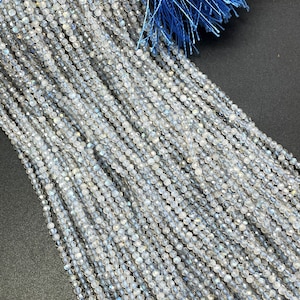 May include: A strand of iridescent white and blue gemstone beads. The beads are round and faceted, creating a shimmering effect. The beads are strung on a clear thread.