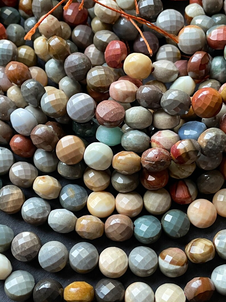 May include: A strand of faceted gemstone beads in various shades of brown, beige, grey, red, and green. The beads are all approximately the same size and have a smooth, polished finish.
