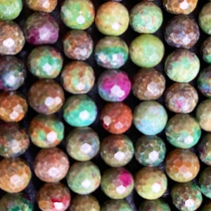 Peut inclure: Un brin de perles rondes en pierres précieuses multicolores. Les perles sont un mélange de vert, de brun et de rose avec des reflets blancs. Les perles sont toutes à peu près de la même taille et sont enfilées sur un fil transparent.