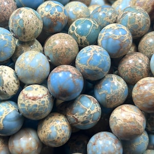 May include: A close-up of a pile of blue and brown jasper beads. The beads are round and have a mottled pattern.