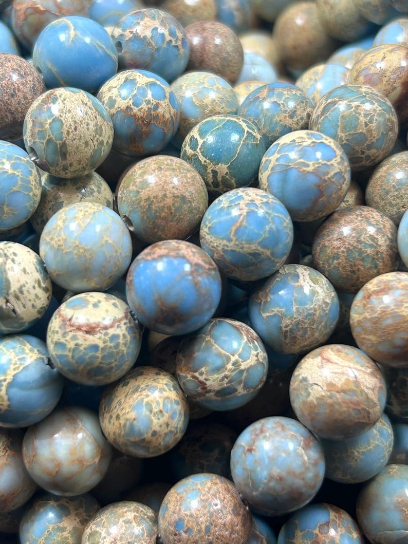 May include: A close-up of a pile of blue and brown jasper beads. The beads are round and have a mottled pattern.