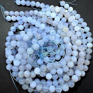 Pu&ograve; includere: Una collana di perle di pietra preziosa di colore azzurro chiaro. Le perle sono rotonde e lisce, e sono infilate su un filo bianco sottile. Le perle sono disposte in un mucchio sciolto, e sono tutte pi&ugrave; o meno della stessa dimensione.