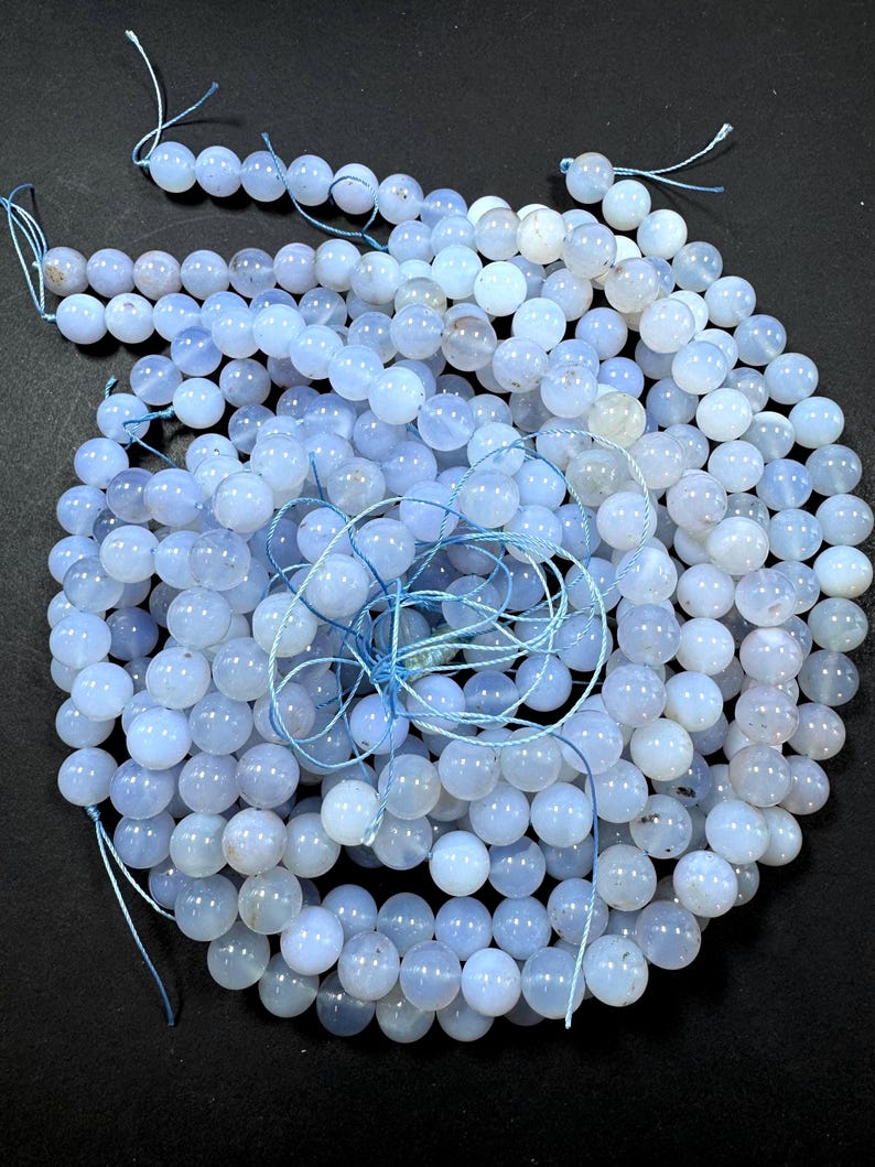 Pu&ograve; includere: Una collana di perle di pietra preziosa di colore azzurro chiaro. Le perle sono rotonde e lisce, e sono infilate su un filo bianco sottile. Le perle sono disposte in un mucchio sciolto, e sono tutte pi&ugrave; o meno della stessa dimensione.