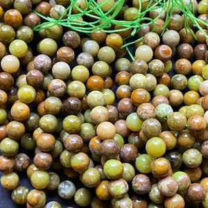 May include: A strand of green, brown, and yellow gemstone beads. The beads are round and have a natural, polished finish.