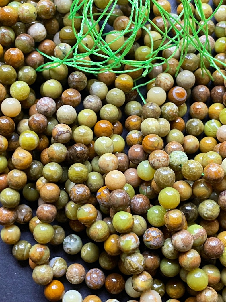 May include: A strand of green, brown, and yellow gemstone beads. The beads are round and have a natural, polished finish.