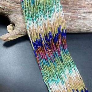 May include: A variety of gemstone beads in different colors, including blue, green, brown, and white, are strung together in long strands. The beads are faceted and have a shiny finish.