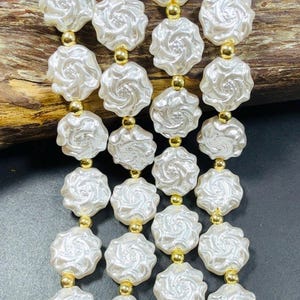 May include: A strand of white pearl beads with a rose design. The beads are separated by gold spacers.