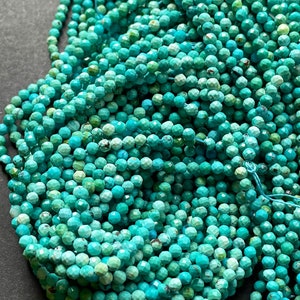 May include: A strand of turquoise gemstone beads, faceted and round, in a vibrant blue-green color. The beads are strung together on a thin thread, creating a long, flowing strand.
