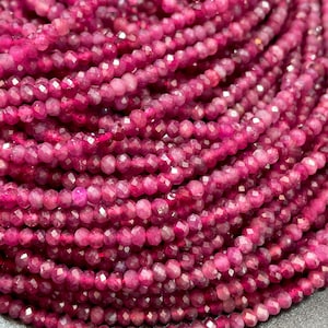 May include: A strand of deep pink ruby beads, faceted and polished, with a smooth, glossy finish. The beads are arranged in a circular pattern, showcasing their vibrant color and intricate facets.