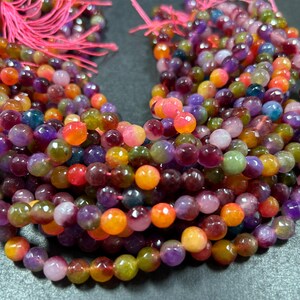 May include: A strand of multi-colored gemstone beads. The beads are round and have a faceted finish. The colors of the beads include purple, green, orange, and pink.
