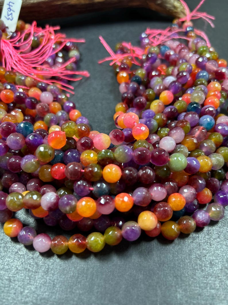 May include: A strand of multi-colored gemstone beads. The beads are round and have a faceted finish. The colors of the beads include purple, green, orange, and pink.