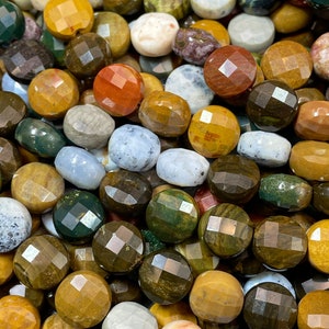 May include: A close-up of a collection of round, faceted gemstone beads in various colors, including green, brown, yellow, white, and red. The beads are made of natural stone and have a polished finish.
