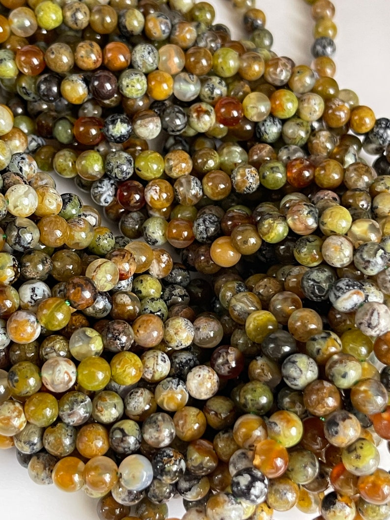 Op de afbeelding: Een streng ronde, groene, bruine en witte agaat kralen. De kralen zijn ongeveer 6 mm in diameter en hebben een natuurlijke, gepolijste afwerking.