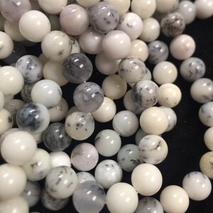 May include: A strand of white and gray opal beads. The beads are round and have a smooth, polished finish. They are perfect for making jewelry or other crafts.