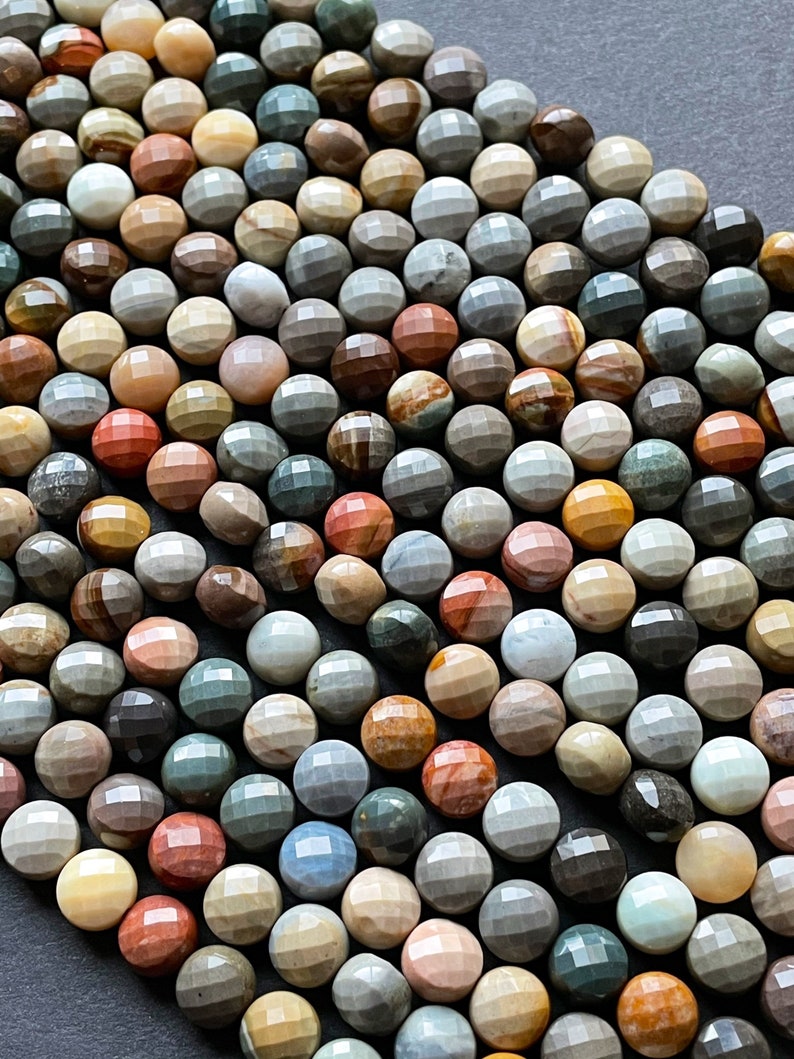 May include: A strand of multi-coloured, faceted gemstone beads. The beads are round and have a variety of brown, grey, red, and yellow tones.