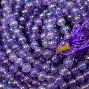 May include: A strand of iridescent purple amethyst beads. The beads are round and have a smooth, polished finish. The beads are strung on a thin, clear thread.