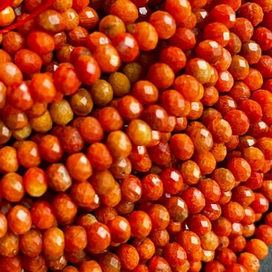 K&ouml;nnte beinhalten: Eine Str&auml;hne aus orangefarbenen und roten Korallenperlen. Die Perlen sind facettiert und haben ein nat&uuml;rliches, organisches Aussehen.