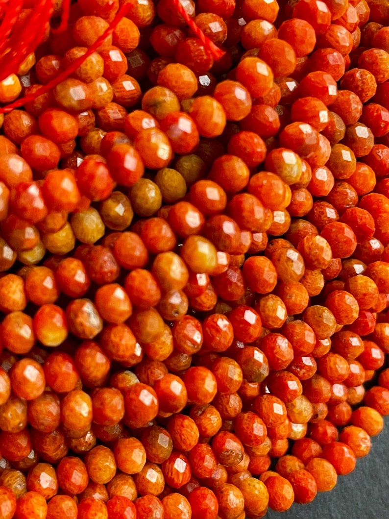 K&ouml;nnte beinhalten: Eine Str&auml;hne aus orangefarbenen und roten Korallenperlen. Die Perlen sind facettiert und haben ein nat&uuml;rliches, organisches Aussehen.