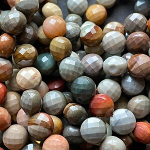 May include: A close-up of a collection of colourful, faceted gemstone beads. The beads are a mix of brown, grey, green, and red tones. The beads are all round and have a smooth, polished finish.