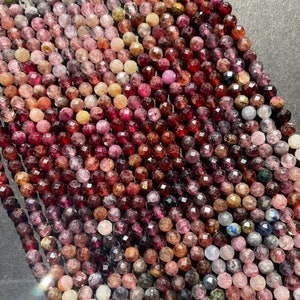 May include: A strand of faceted gemstone beads in various shades of pink, red, and brown. The beads are round and have a slightly irregular shape.