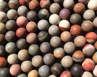 May include: A collection of colorful, round, smooth, polished stones. The stones are various shades of brown, red, gray, and white. The stones are arranged in a close-up, flat lay pattern.