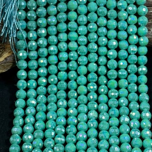 May include: A strand of teal green faceted glass beads. The beads have a iridescent finish.