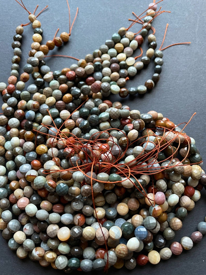 May include: A strand of multi-coloured gemstone beads, featuring a variety of shades of brown, grey, and red. The beads are faceted and have a smooth, polished finish.