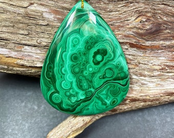 May include: A green malachite pendant with a teardrop shape and intricate swirling patterns. The pendant is hanging from a gold cord.