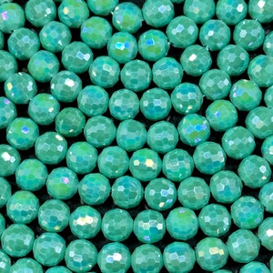 May include: A close-up of a strand of iridescent teal green faceted beads. The beads are round and have a smooth, polished finish.