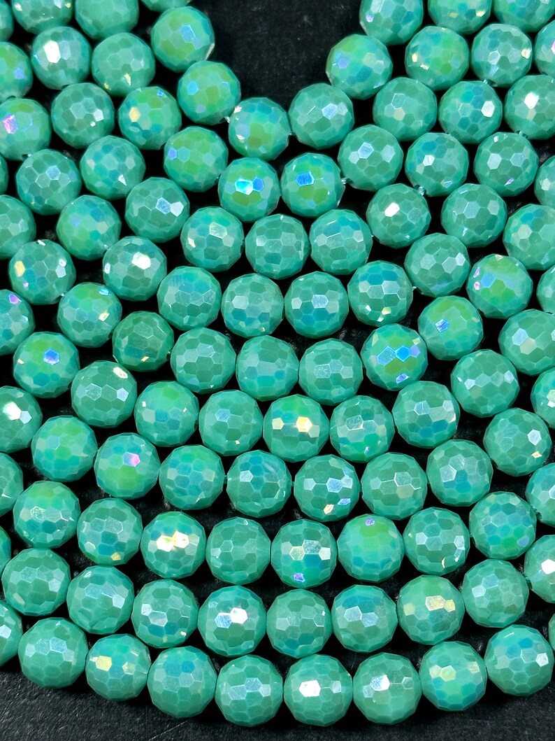 May include: A close-up of a strand of iridescent teal green faceted beads. The beads are round and have a smooth, polished finish.