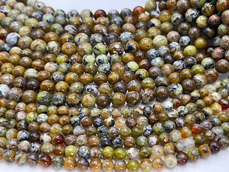 Op de afbeelding: Een streng ronde, groene, bruine en witte opaal kralen. De kralen zijn ongeveer 6 mm in diameter en hebben een natuurlijk, onregelmatig patroon.