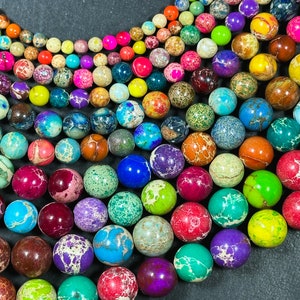 May include: A collection of colorful, round beads in various sizes and shades, including red, green, blue, purple, and yellow. The beads have a speckled, marbled appearance, suggesting they are made of stone or a similar material. The beads are arranged in a curved pattern.