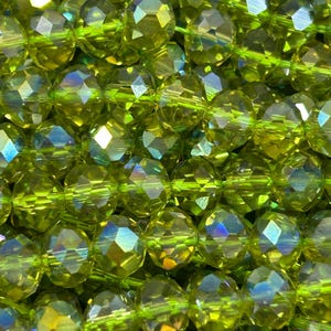 May include: A strand of faceted green glass beads with iridescent shimmer. The beads are round and have a faceted design.