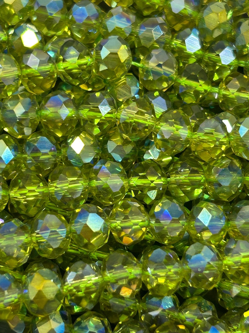 May include: A strand of faceted green glass beads with iridescent shimmer. The beads are round and have a faceted design.
