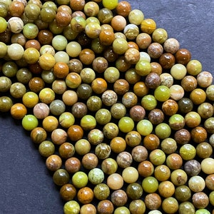 May include: A strand of round, green, brown, and yellow opal beads. The beads are approximately 6mm in diameter and have a smooth, polished finish.