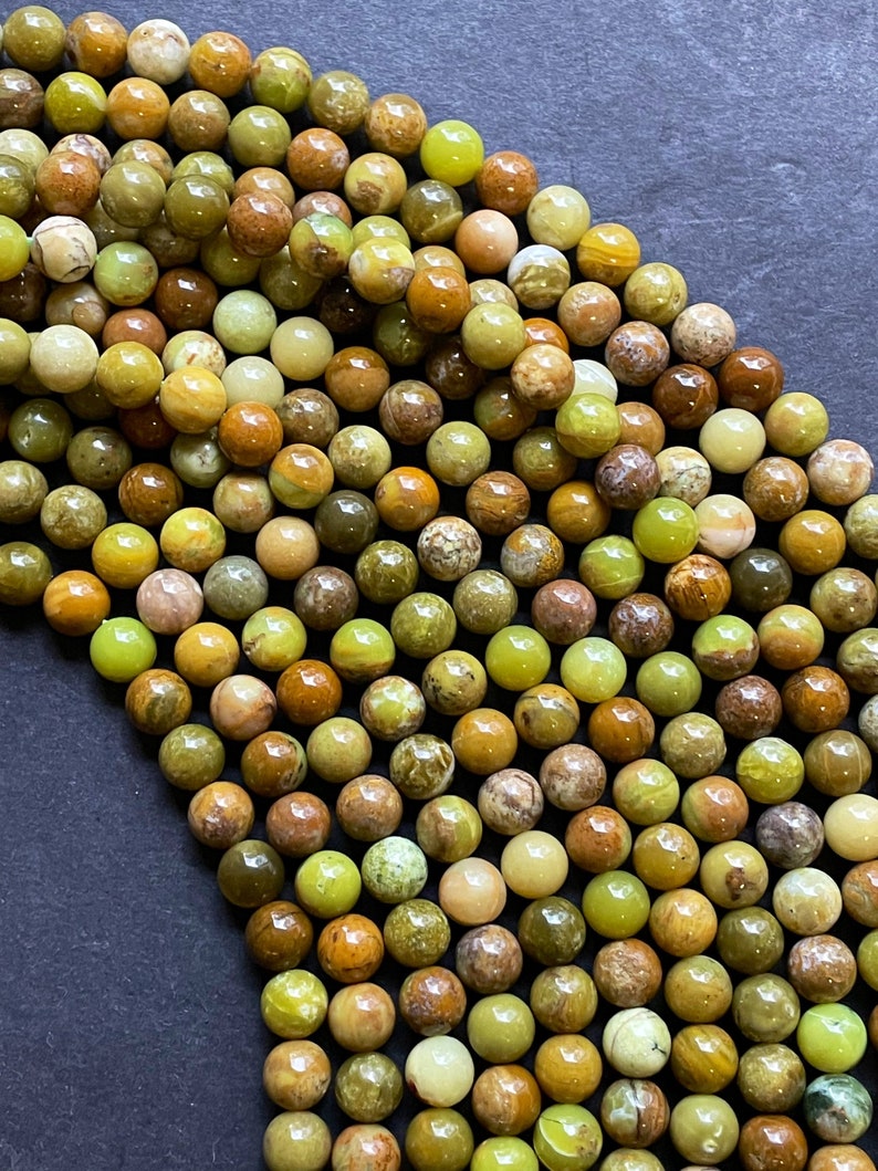 May include: A strand of round, green, brown, and yellow opal beads. The beads are approximately 6mm in diameter and have a smooth, polished finish.