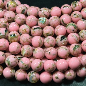 May include: Close-up of a collection of pink gemstone beads. Each bead is round with a polished finish and features a unique pattern of green, white, and gold-colored inclusions. These beads are ideal for jewelry making and crafting.