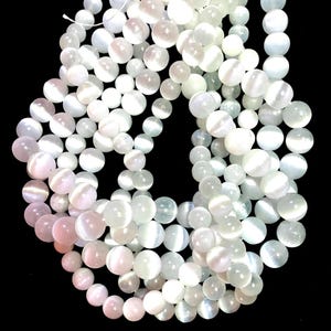 May include: A strand of white gemstone beads with a iridescent sheen. The beads are round and smooth, and they are strung on a clear thread.