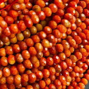 K&ouml;nnte beinhalten: Eine Str&auml;hne orangefarbener Korallenperlen. Die Perlen sind facettiert und haben ein nat&uuml;rliches, organisches Aussehen.
