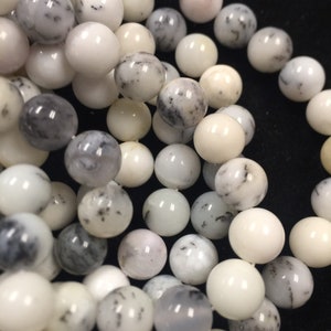 May include: A close-up of a strand of white and gray opal beads. The beads are round and smooth, with a variety of patterns and textures.