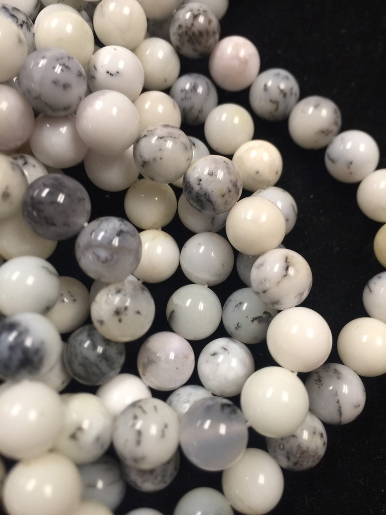 May include: A close-up of a strand of white and gray opal beads. The beads are round and smooth, with a variety of patterns and textures.